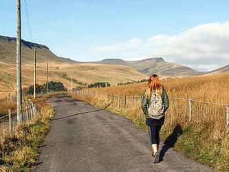 redheaded girl walking down a rural path with rolling hills in the background